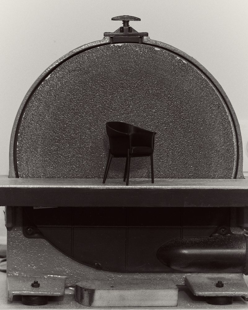 Monochromatic shot of a modern chair centered against a round, textured surface, set on a gray, speckled industrial machine.