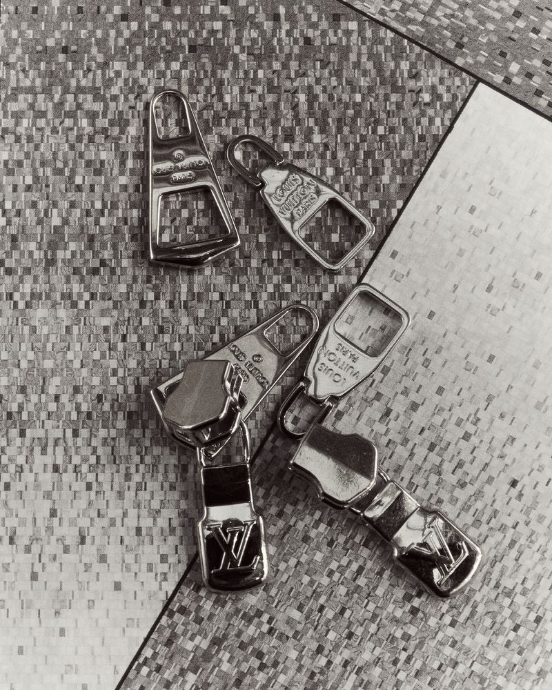 Monochrome shot of four Louis Vuitton zipper pulls on a textured surface, showcasing luxury fashion accessories in a studio setting.
