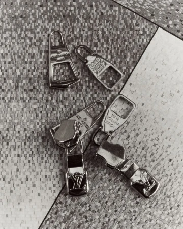 Monochrome shot of four Louis Vuitton zipper pulls on a textured surface, showcasing luxury fashion accessories in a studio setting.