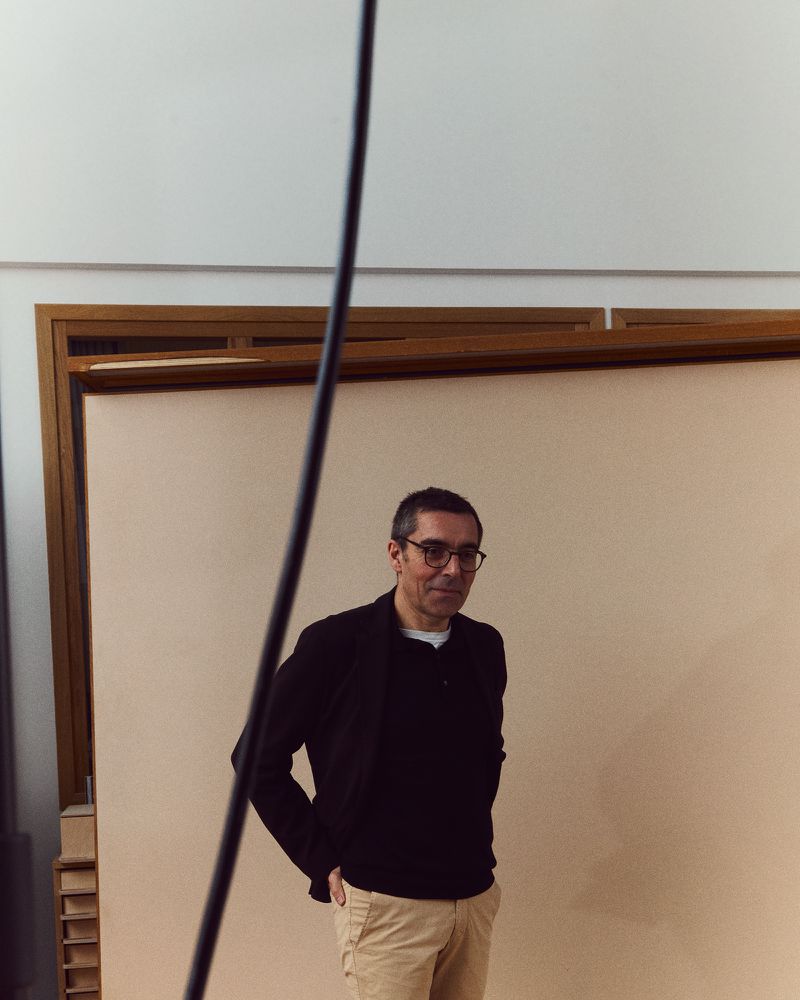 Portrait of an adult male in glasses, wearing a dark blazer and khaki pants, in a photo studio with neutral background.