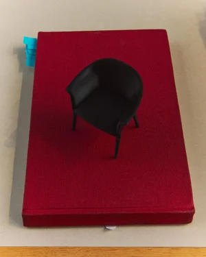 Miniature black armchair placed on top of a rectangular red book against a neutral surface