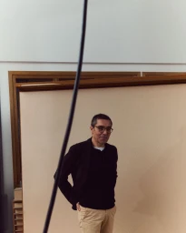 Middle-aged man wearing glasses, dark blazer, and beige trousers standing in an interior space for Port Magazine.