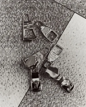 Close-up overhead view of polished metal zipper pulls arranged on a textured patterned tile surface.