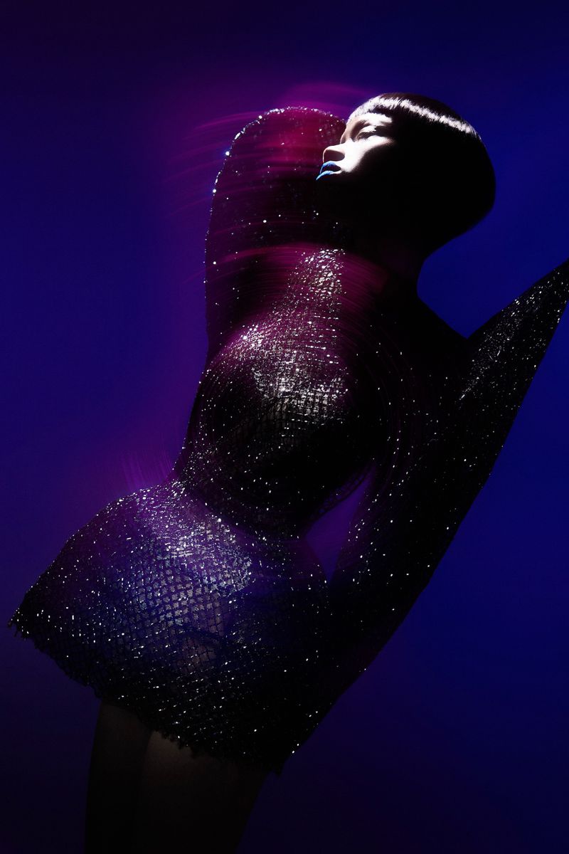 Fashionable woman in sparkling dress posing in front of blue backdrop with pink accents. Head and shoulders shot in studio lighting.