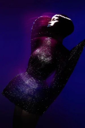 Fashionable woman in sparkling dress posing in front of blue backdrop with pink accents. Head and shoulders shot in studio lighting.