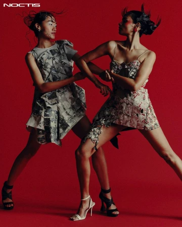 Two fashion models in patterned mini-dresses strike dynamic poses against a vibrant red backdrop, showcasing modern style and design.