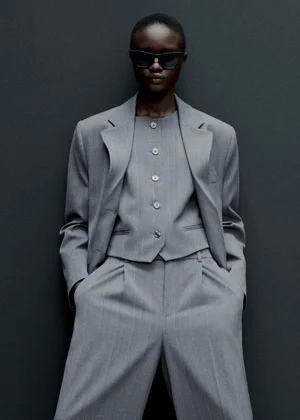 Model wearing a grey pinstripe suit, matching vest, and dark sunglasses against a dark textured background for Mango Office Wear
