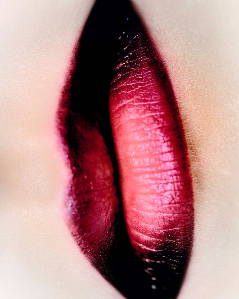 Close-up of dark red lipstick on human lips with blurred background showing detail of texture, color, and form in beauty shot.