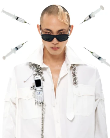 Portrait of a person with a shaved head wearing sunglasses and a white shirt, accessorized with repurposed flip phone on a white backdrop.