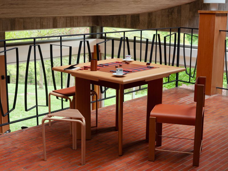 Interior view of a home with a game table set up for checkers on a brick floor near a black metal railing with wooded scenery.