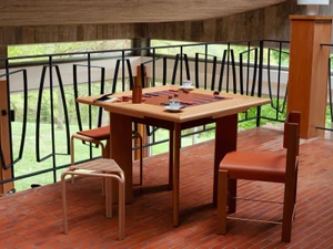Wooden game table set up on a tiled balcony with chairs and a black metal railing overlooking trees.