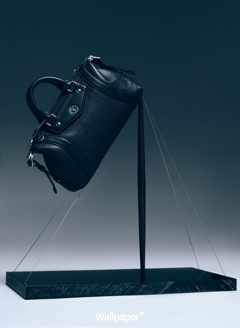 Studio shot of a black leather handbag, presented on a marble display stand, with thin cords giving the illusion of levitation.