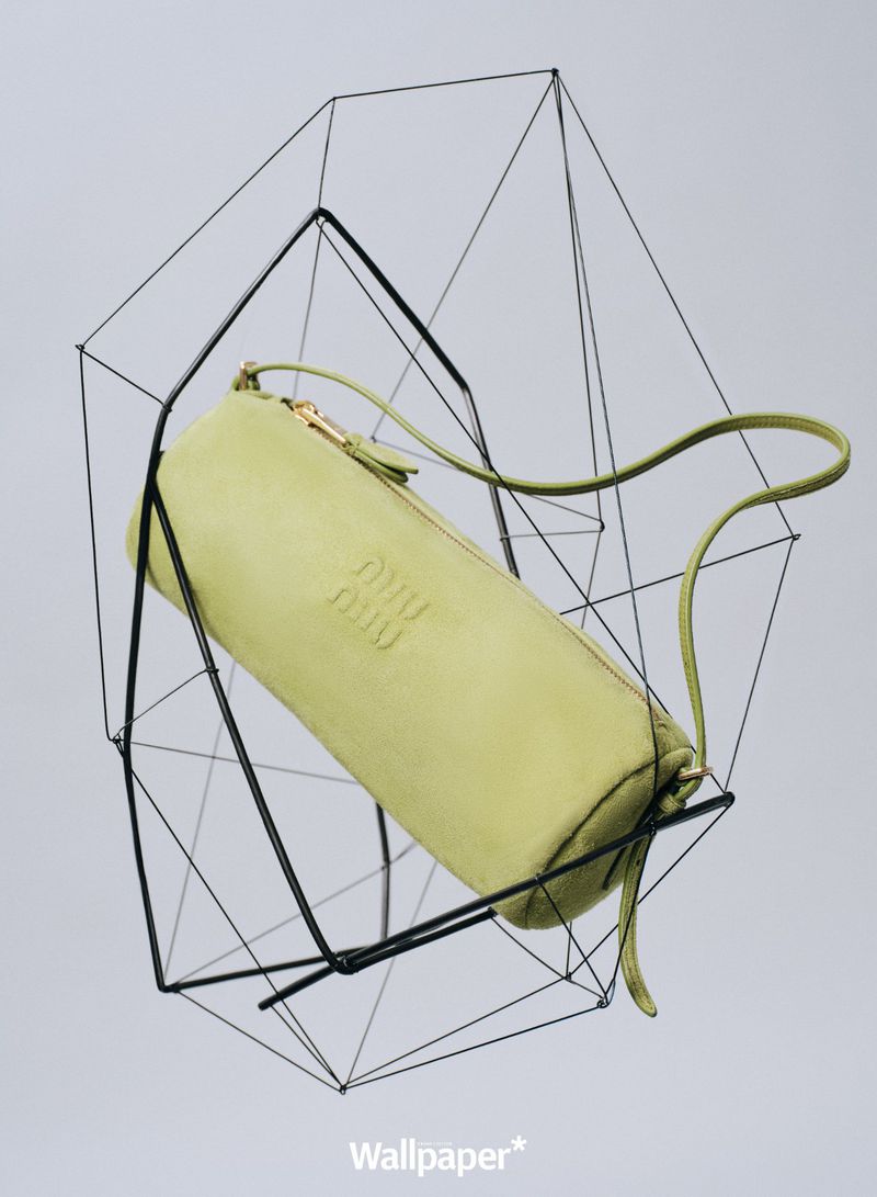 Fashion still life showcases a pale green purse in a black geometric wire frame against a gray background, embodying modern elegance.