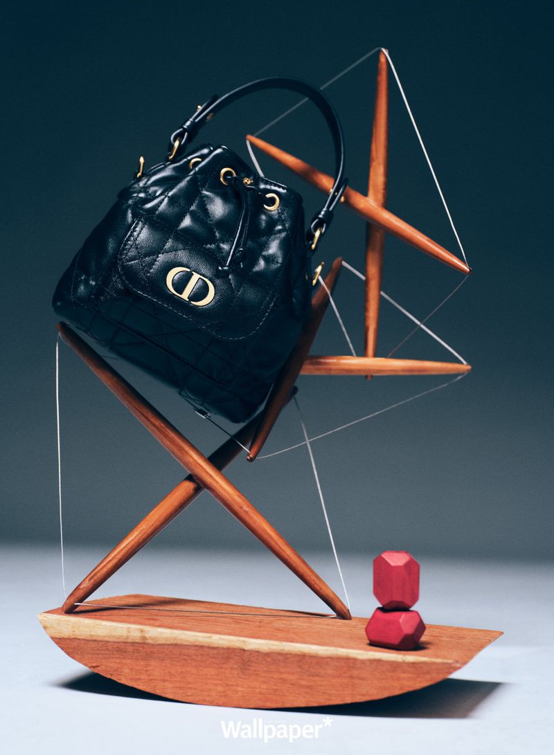Elegant black quilted leather bucket bag with gold logo hardware displayed on a wooden geometric stand against a dark grey background.