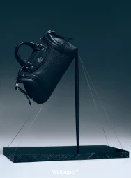 A black leather handbag balanced diagonally on a dark thin stand against a cool grey gradient background for Wallpaper China.