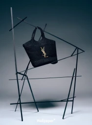 Black woven handbag with gold YSL logo hanging on an abstract dark metal wire sculpture