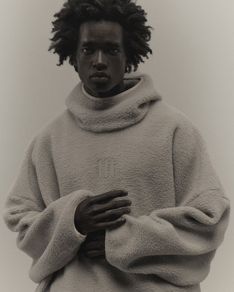 Portrait of a dark-skinned adult man with afro hair, wearing a high neck fleece sweater in a neutral indoor setting.