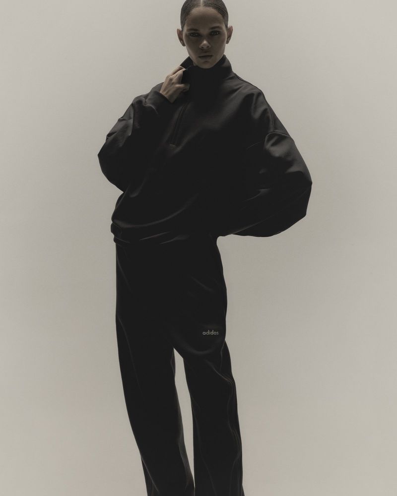 Young woman in a relaxed pose in an indoor setting. She is wearing an oversized black top and pants. Studio lighting with a neutral background.