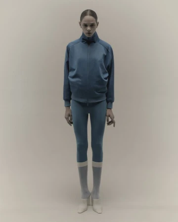 Model in a blue athletic zip jacket and leggings standing against a neutral studio background