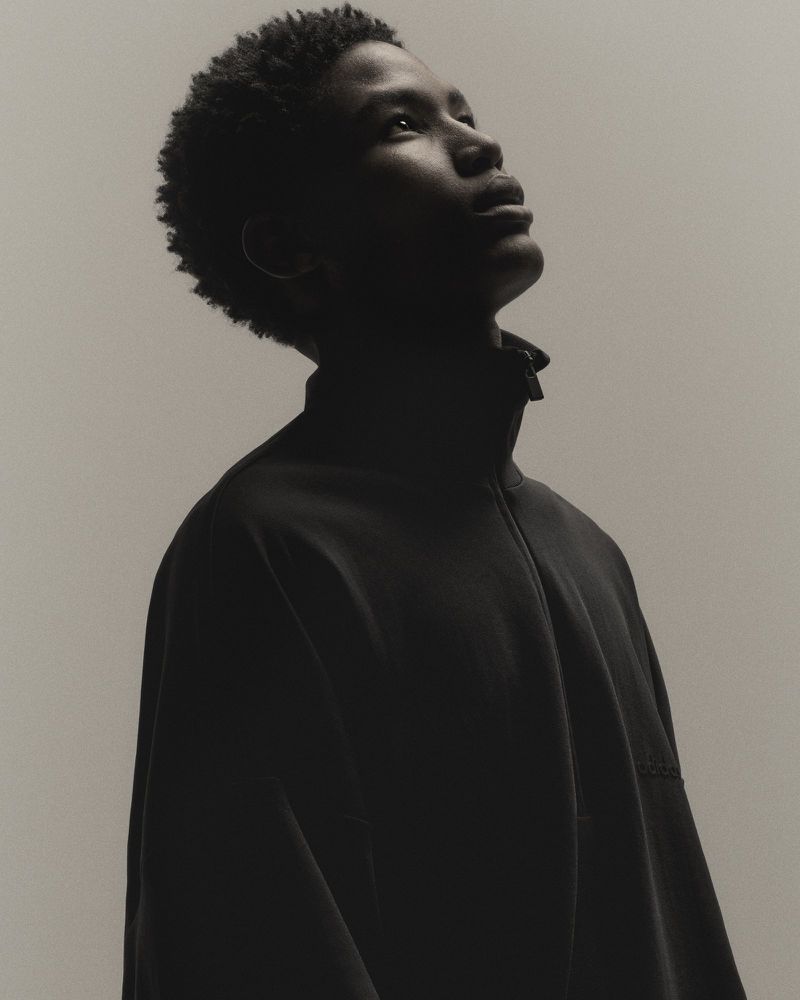 Portrait of an adult male wearing a black jacket looking upward, set against a light neutral background in an indoor studio environment.