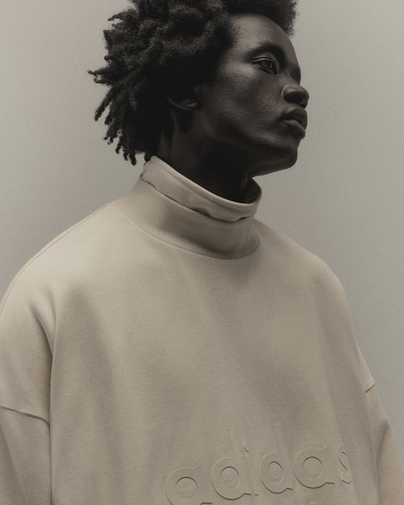 Portrait of an African-American man with dark curly hair wearing a beige high-neck sweatshirt, captured in a photo studio setting.