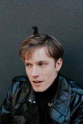 Actor Louis Hofmann with a chess piece on his head wearing a black leather jacket against a dark background