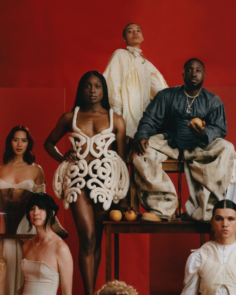 Group shot of diverse people in fashionable outfits against a red backdrop, showcasing unique textures, tones, and creative design elements.