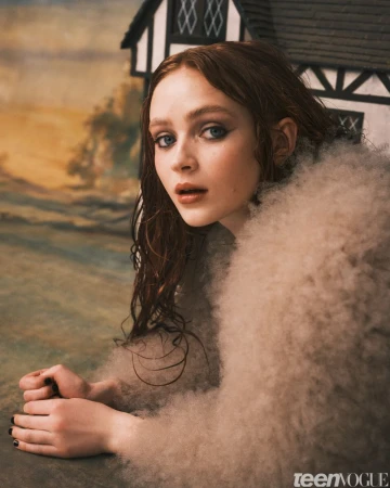 Close-up portrait of a young woman with auburn hair, wearing a cream-colored, fluffy jacket, posing in front of a rustic, illustrated backdrop.