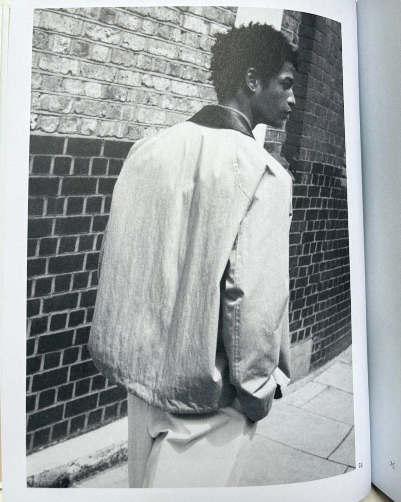 Monochrome image of a man wearing a jacket against a brick wall, creating an urban fashion editorial style photograph.