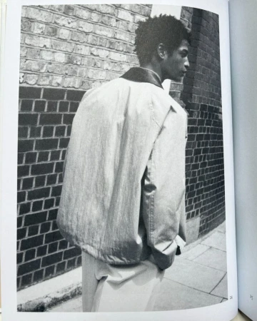 Monochrome image of a man wearing a jacket against a brick wall, creating an urban fashion editorial style photograph.