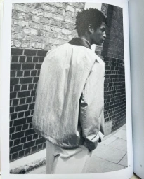 Black and white editorial portrait of a male model wearing a light jacket standing in front of a brick wall.