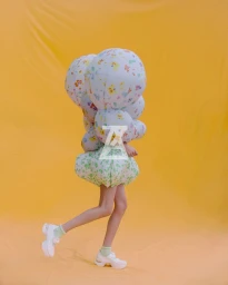Model wearing a voluminous floral patterned outfit with spherical shapes against a yellow backdrop