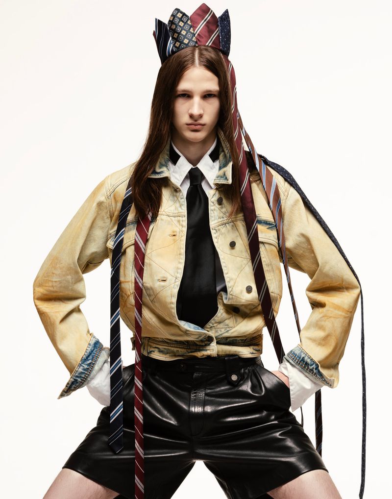 Person in fashion shot with a tie crown and tie details, wearing denim jacket and black shorts against a white backdrop.