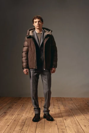 Man in gray suit and brown puffer jacket stands against gray background on wood floor in studio lighting. Fashion photography.