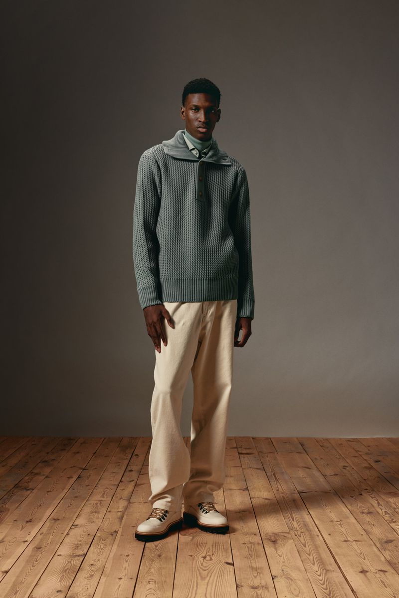 Full shot of a Black male model in a ribbed sweater and khaki pants on a wooden floor in a studio, fashion photography, studio lighting.