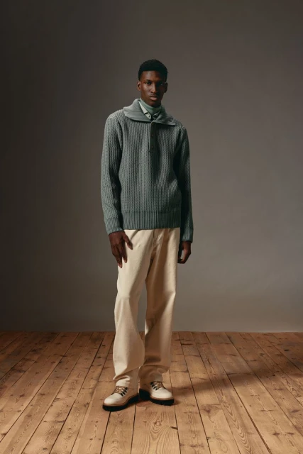 Full shot of a Black male model in a ribbed sweater and khaki pants on a wooden floor in a studio, fashion photography, studio lighting.