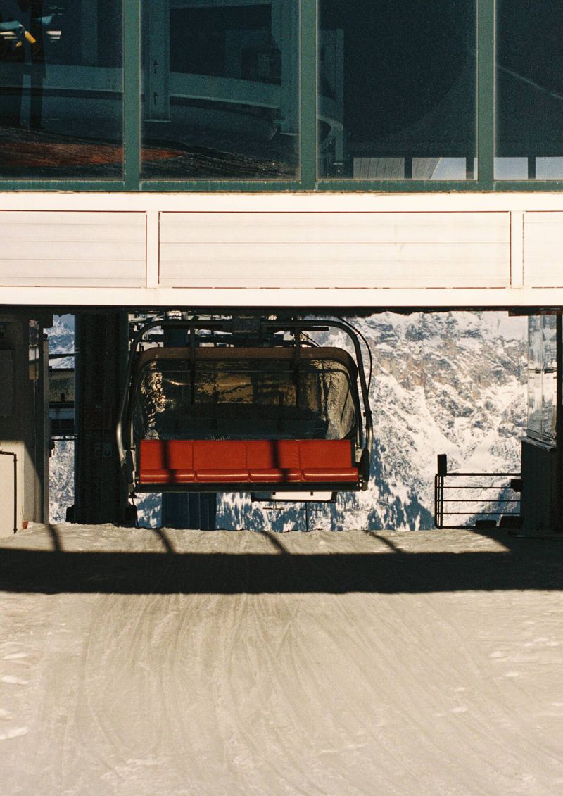 An outdoor shot showcases a stationary, red chairlift at the station, set against a backdrop of snowy mountains and a partly visible building.