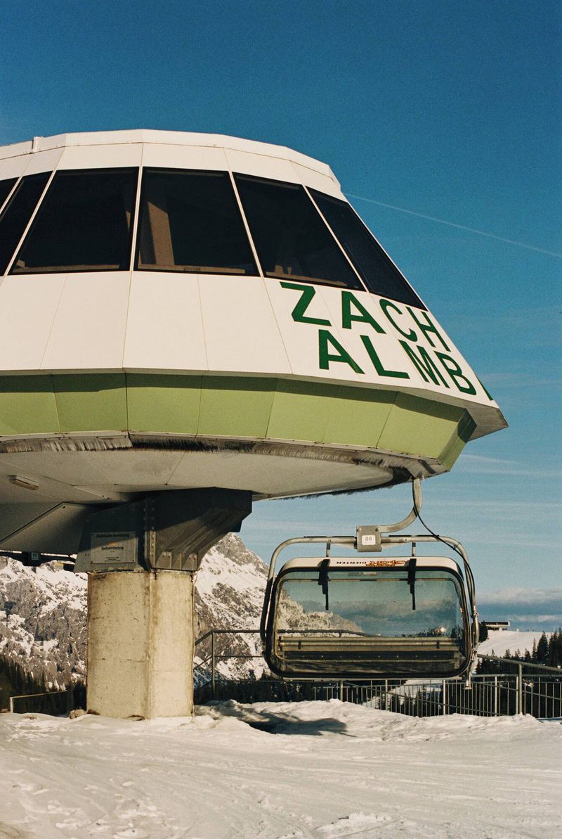 Ski lift station in a snowy mountain landscape under a clear blue sky, featuring a chairlift and mountain peak backdrop.