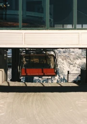 Ski lift chair with red seating positioned at a mountain station above a snow covered slope.
