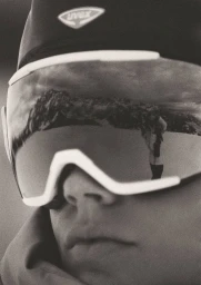 Close-up portrait of model Lois Schindeler wearing ski goggles with a mountain landscape reflected in the visor.