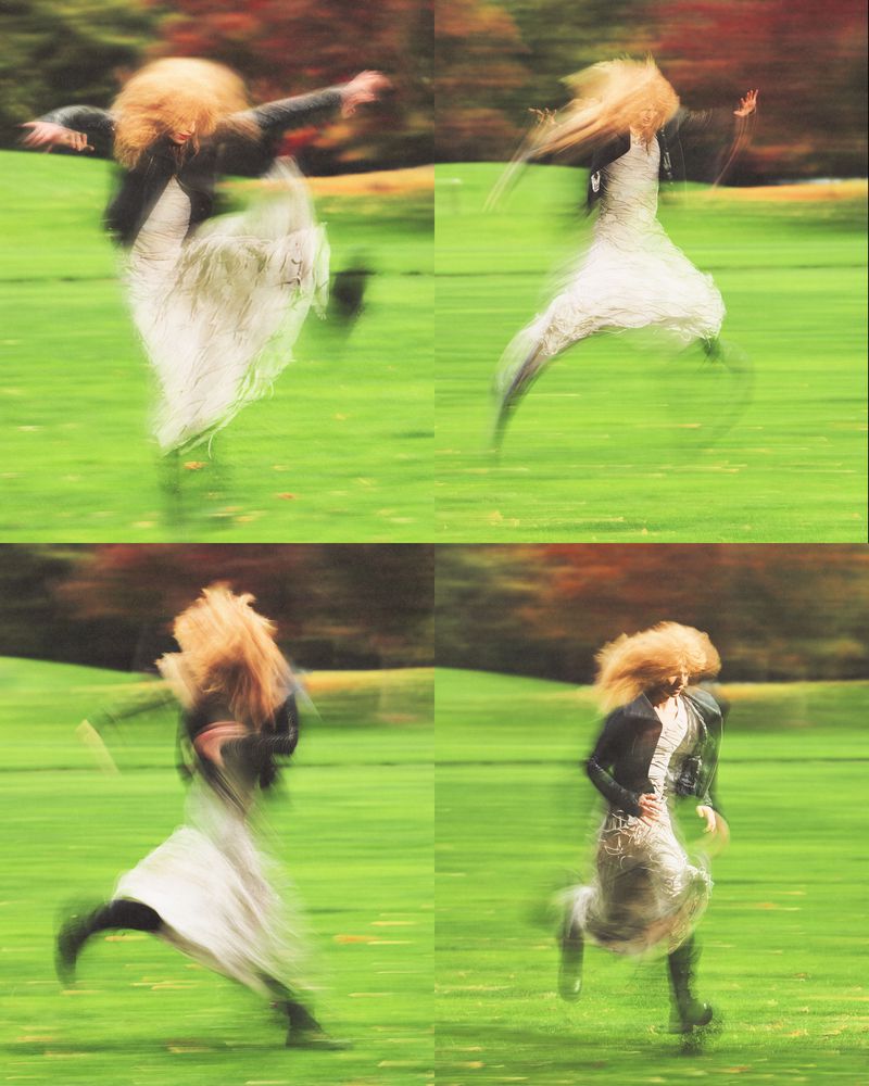 Woman with long hair in flowing dress and boots captured in motion blur in four frames of running on green grass near trees.