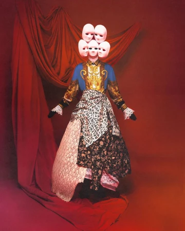 Fashion editorial featuring a mannequin wearing a blue and gold jacket, skirt of mixed fabrics, and cluster of masks for a headpiece.
