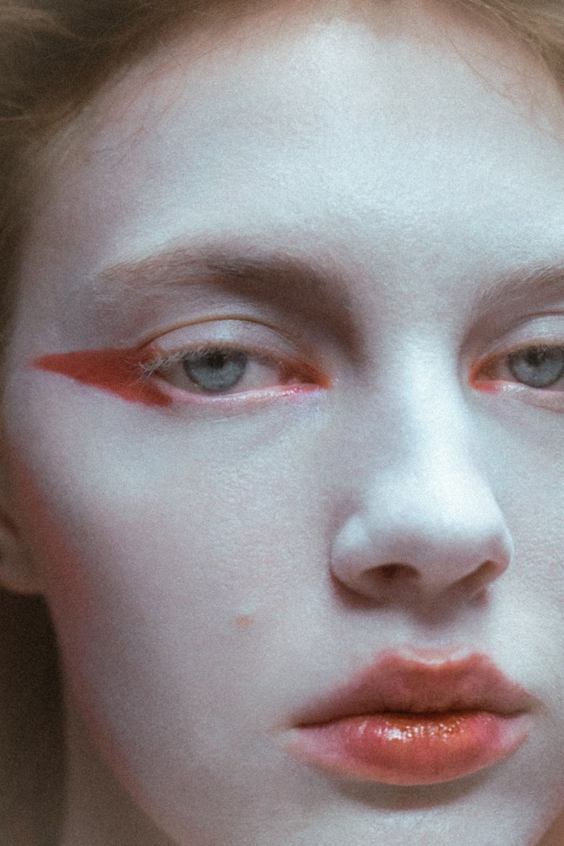 Close-up studio portrait of a young adult female with red eyeliner and glossy red lips, showcasing beauty and fashion-inspired makeup.