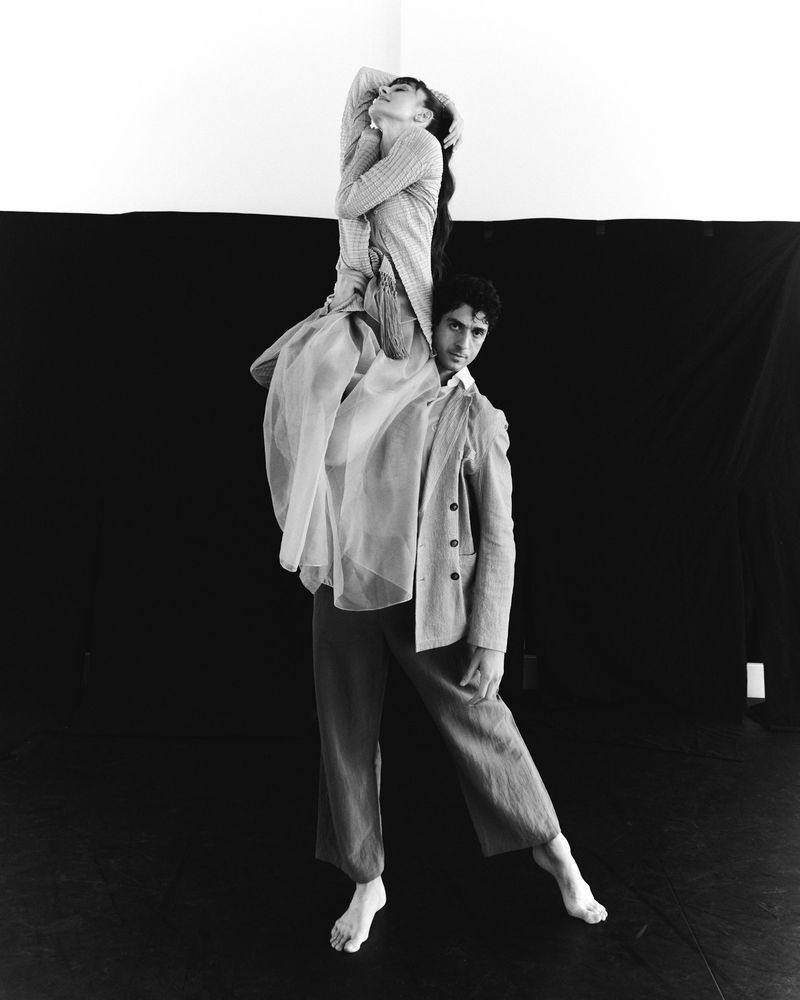 Monochromatic shot of two figures, one adult male carrying an adult female on his shoulders against a black and white backdrop.