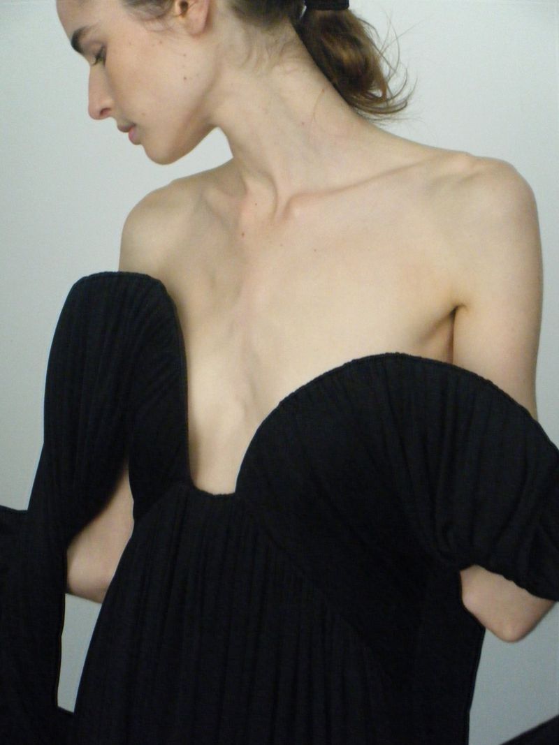 Elegant woman in a black dress with a plunging neckline, captured in a close-up studio shot with soft lighting and a minimalist aesthetic.