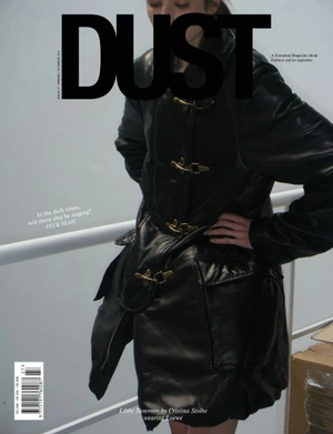Model wearing a black leather coat with brass toggle clasps on a magazine cover against an off-white wall with a railing.