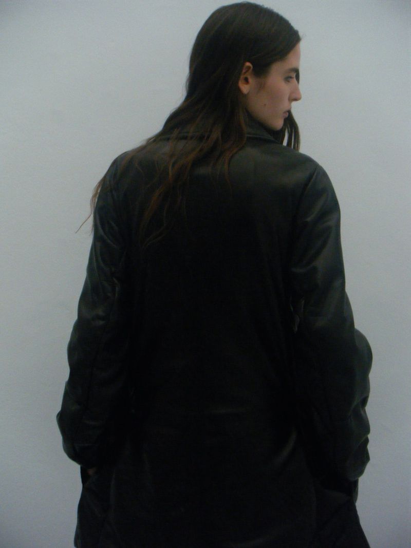 Model in a dark coat viewed from behind against a plain grey background for Dust Magazine editorial