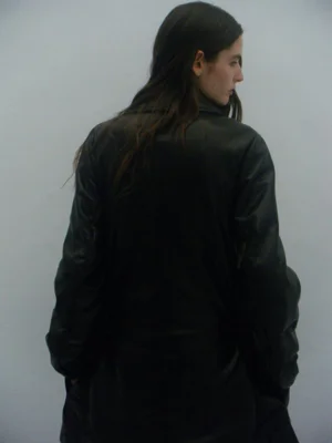 Model in a dark coat viewed from behind against a plain grey background for Dust Magazine editorial