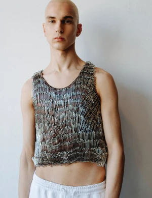 Close-up portrait of a male model wearing a sleeveless top made of safety pins against a white background
