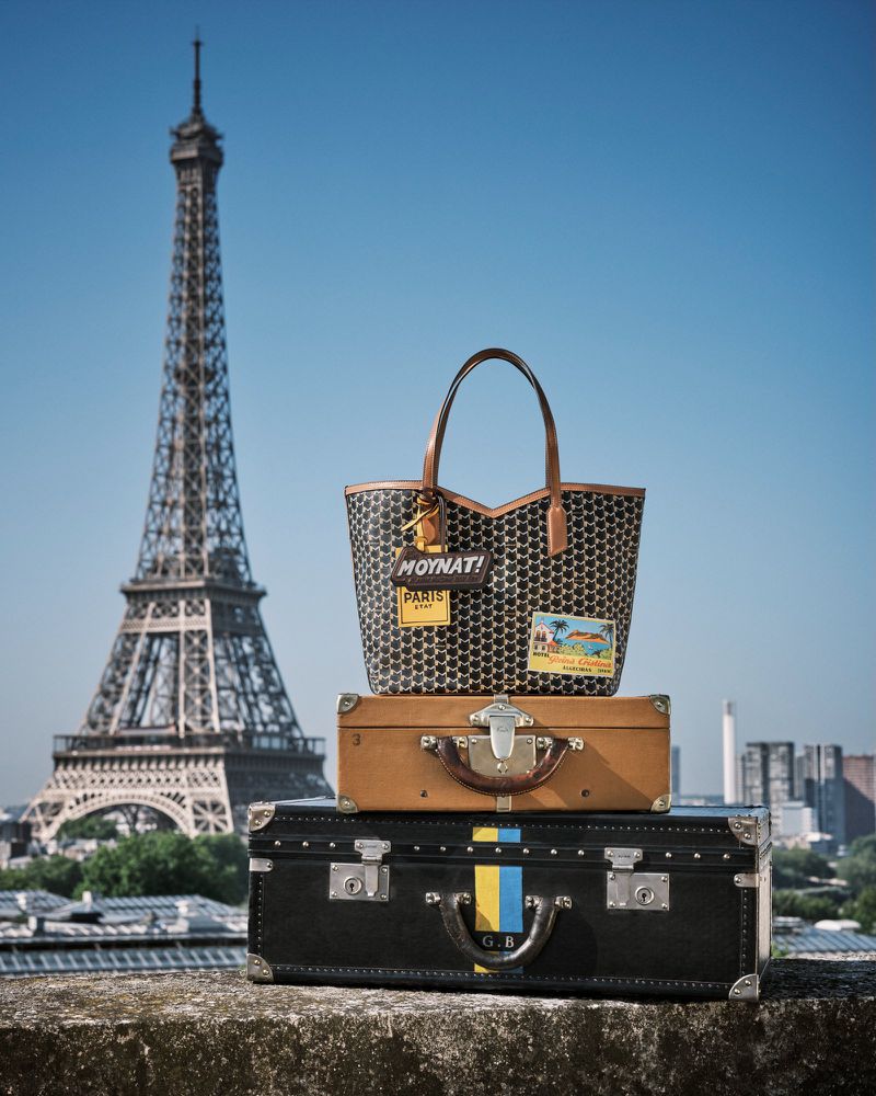 Vintage luggage and designer handbag stacked with the Eiffel Tower in the background, evoking travel and Parisian style.